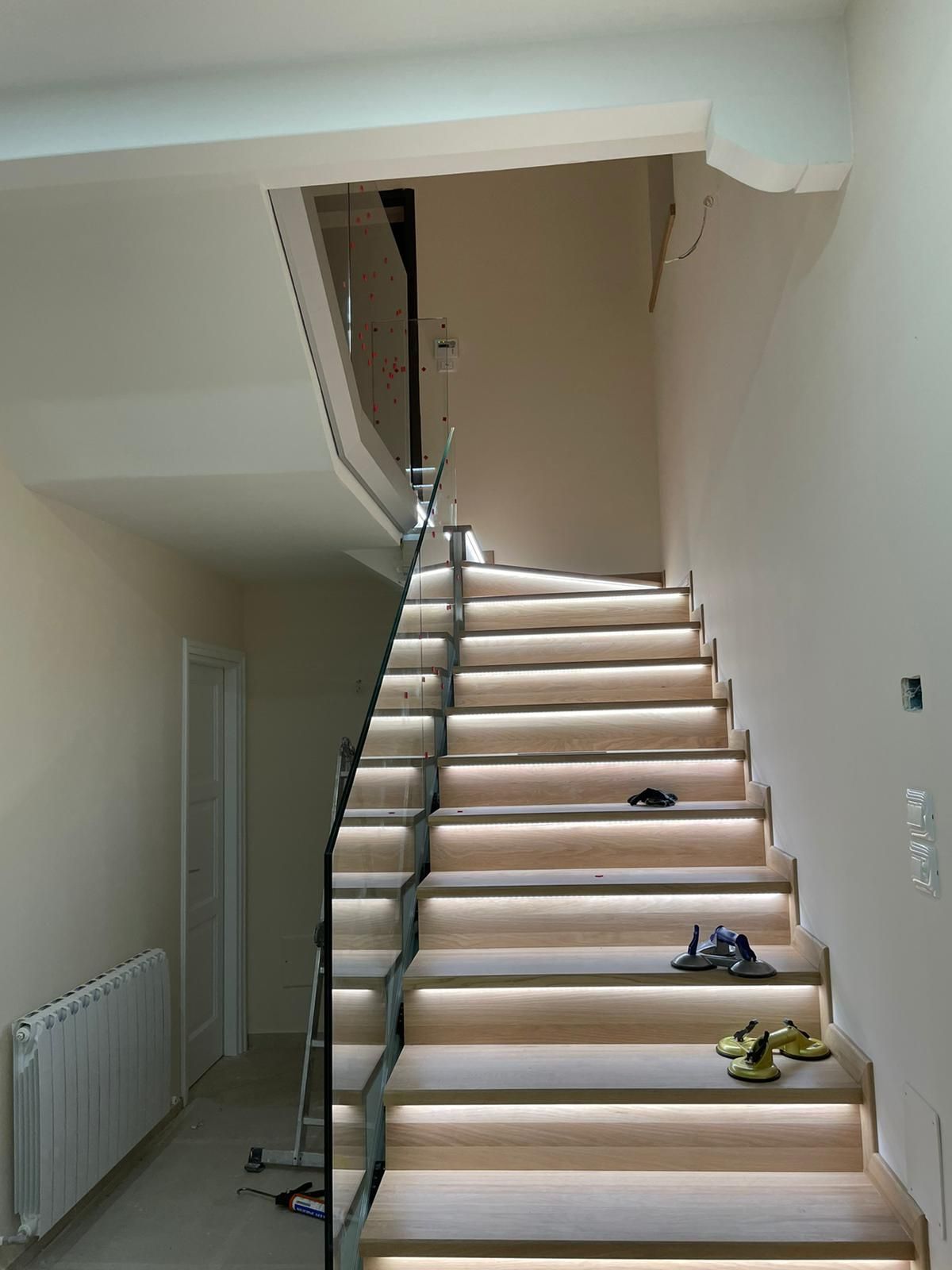 Scala con gradini in legno e ringhiera in vetro. Luci a LED illuminano i gradini. Le pareti sono di colore chiaro.