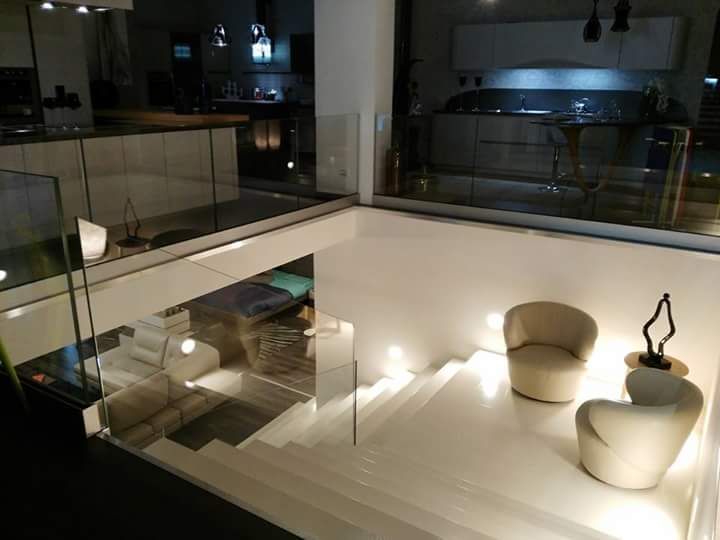 Interni moderni con scale bianche, ringhiere in vetro e zona salotto. La cucina è visibile sullo sfondo.