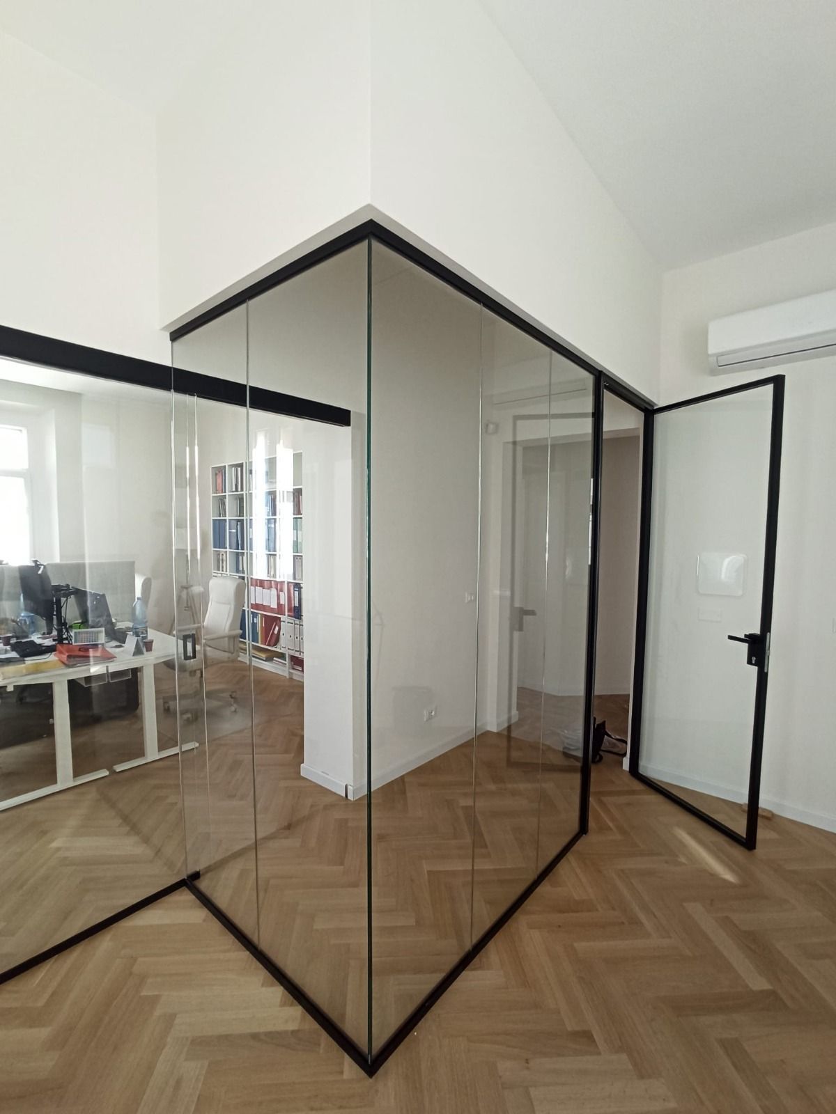 Ufficio con pareti in vetro, infissi e porta neri. Vista interna con scrivania e libreria a vista.