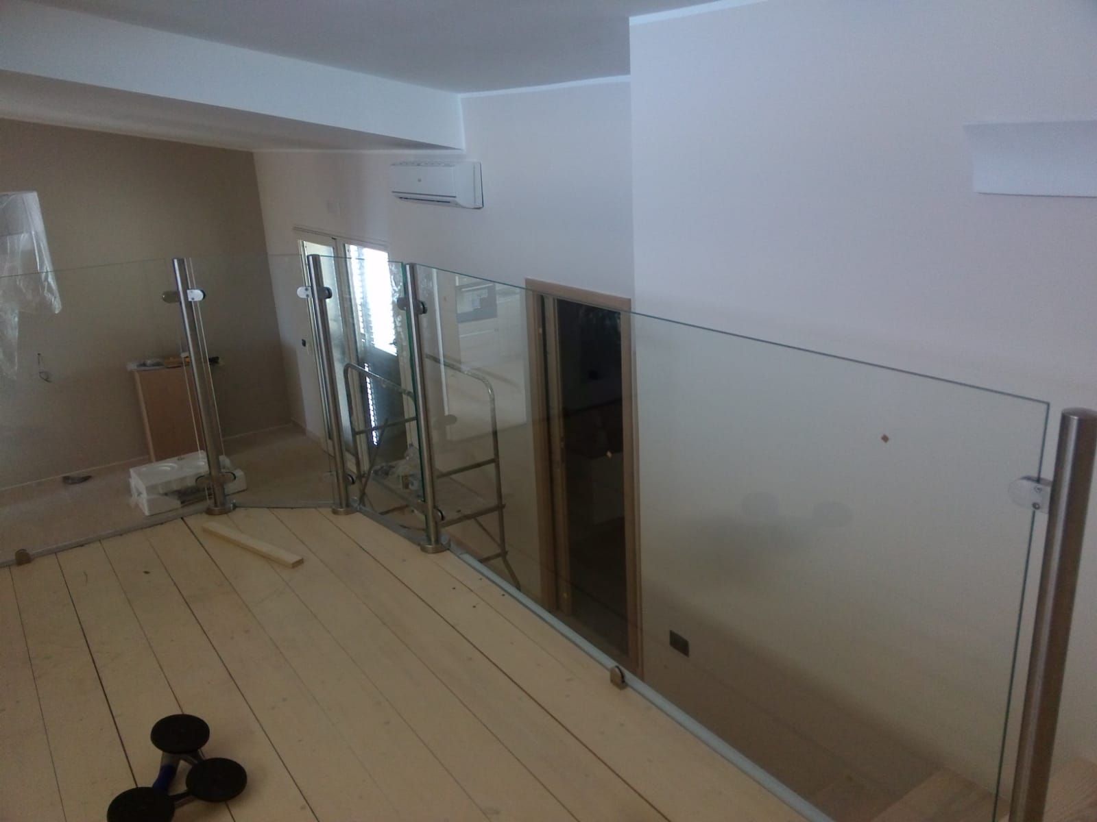 Scena di costruzione di interni. Una stanza parzialmente rifinita con pavimento in legno, ringhiera in vetro e una porta.