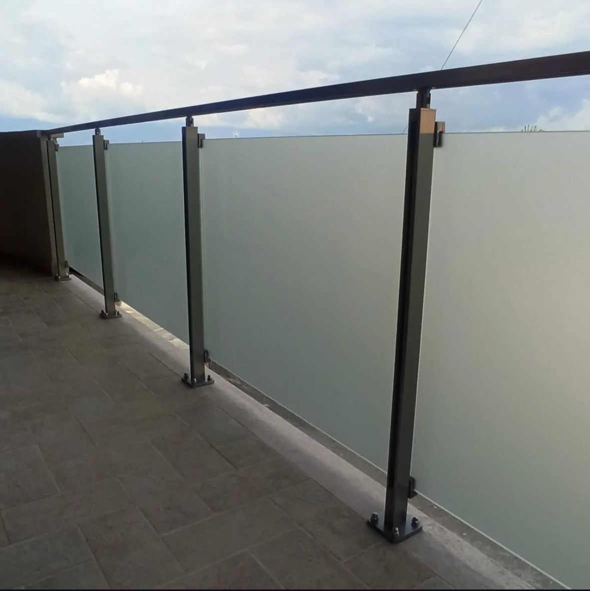 Ringhiera del balcone in vetro smerigliato con pali e corrimano in metallo nero, all'esterno.