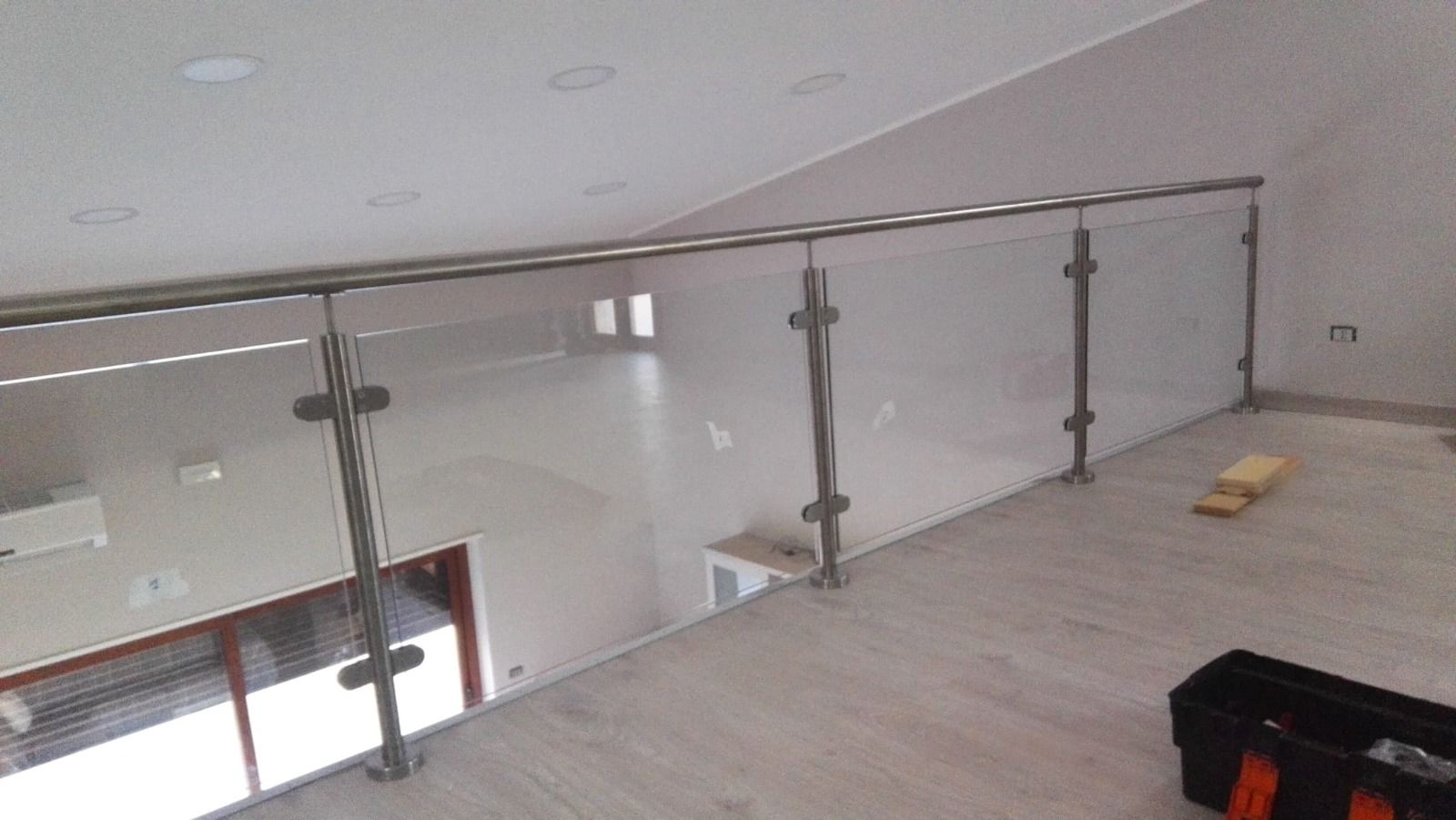 Ringhiera in acciaio inossidabile e vetro sul pianerottolo del secondo piano che si affaccia su una stanza piena di luce.