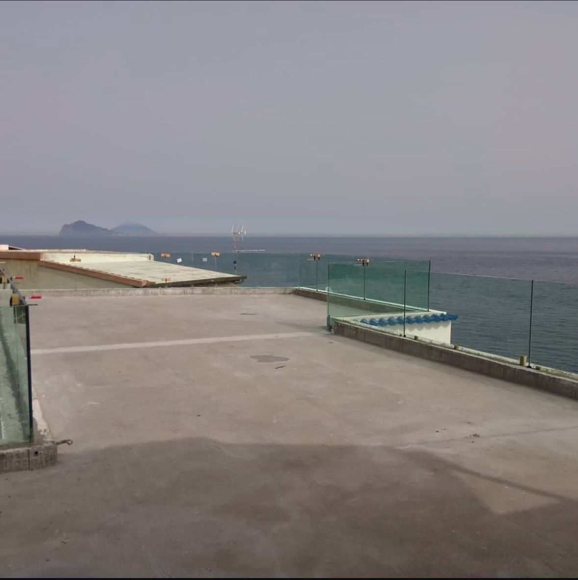 Terrazza panoramica in cemento con vista sull'oceano e ringhiere in vetro.