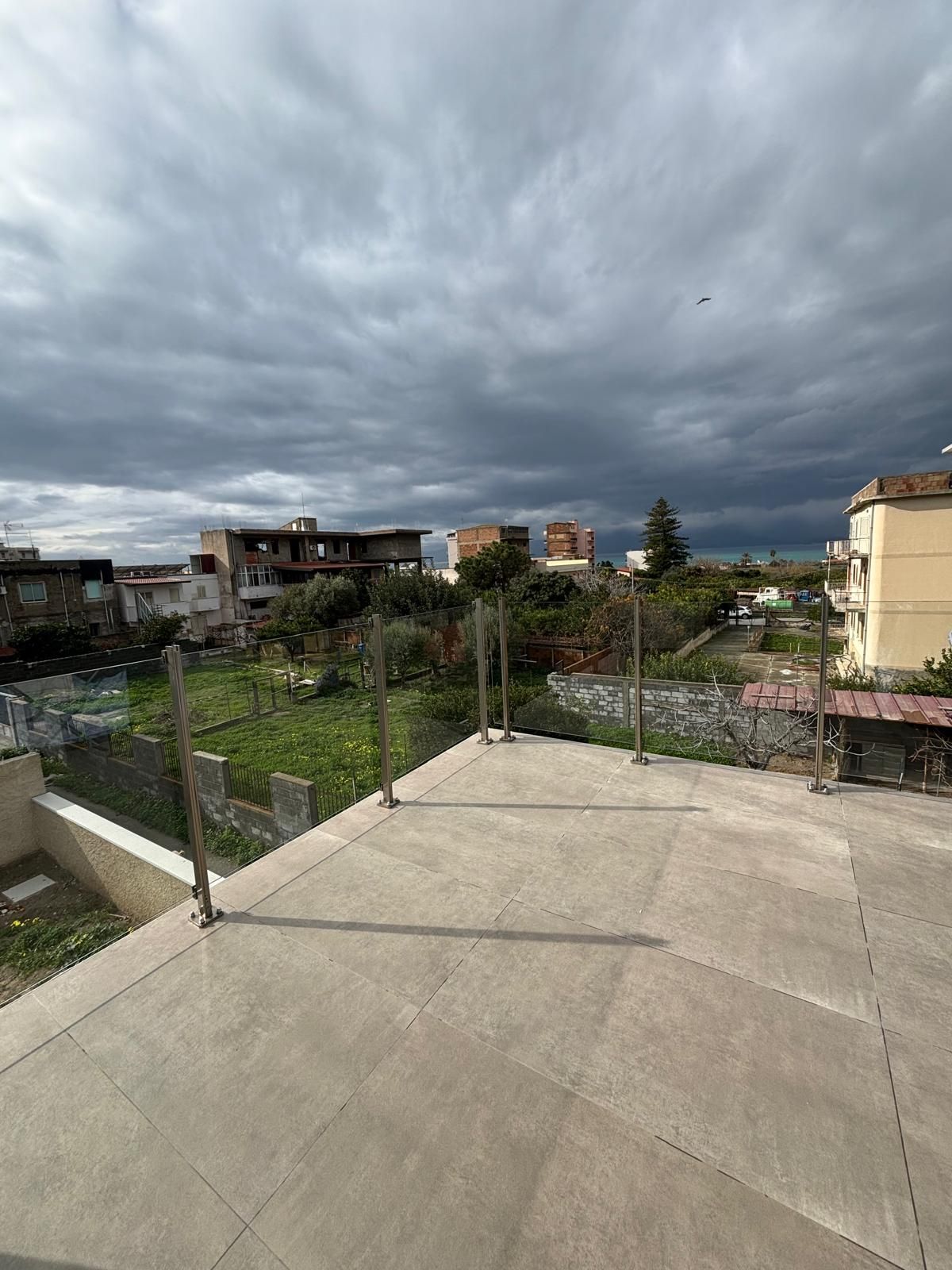 Vista da un tetto: ringhiere in acciaio inossidabile, cielo coperto, edifici in lontananza.