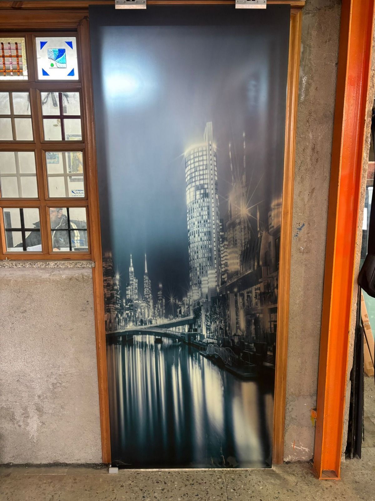 Porta con grafica di paesaggio urbano; ponte ed edifici riflessi nell'acqua, ambientazione notturna.