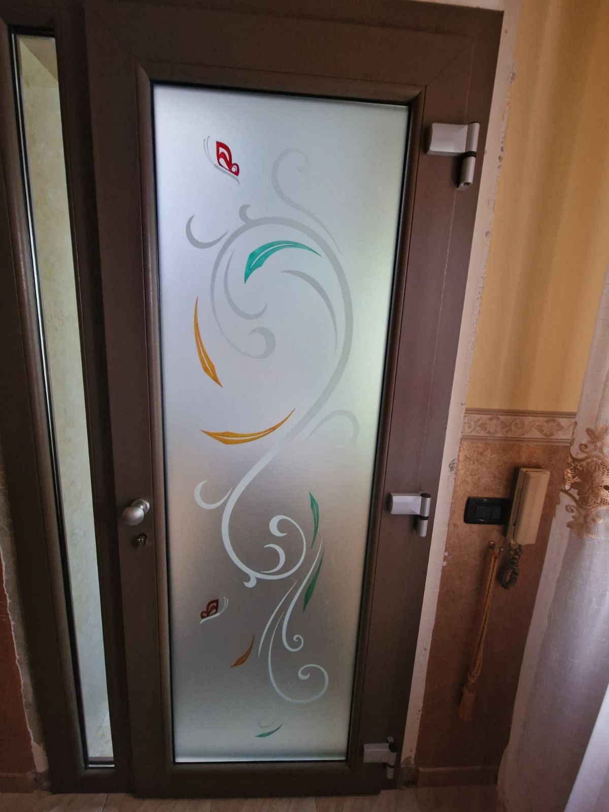 Porta marrone con pannello in vetro smerigliato, decorata con motivi di foglie e farfalle colorate.