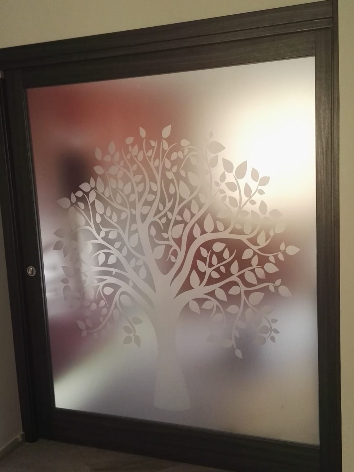 Porta in vetro smerigliato con motivo ad albero bianco. Telaio marrone, illuminazione soffusa.