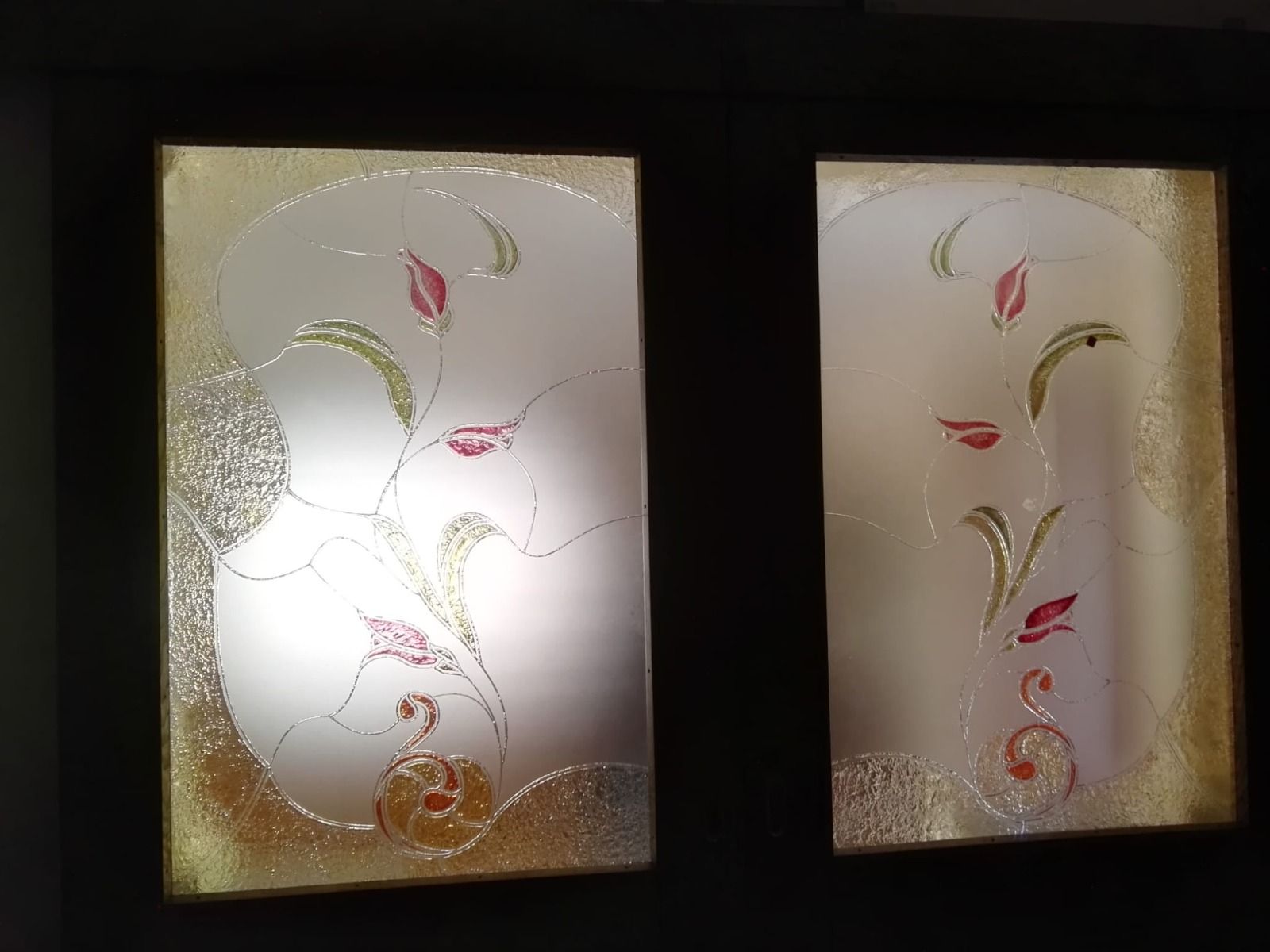 Due pannelli in vetro con motivo floreale; finiture dorate, sfondo bianco satinato, dettagli rossi e verdi.