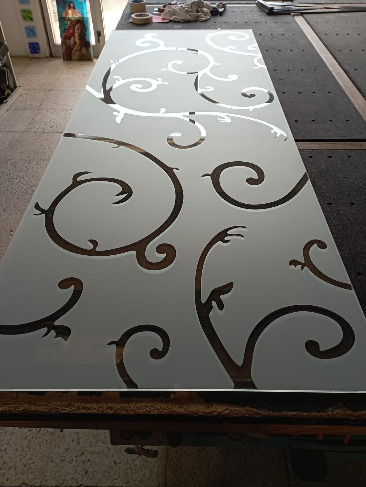 Pannello in vetro smerigliato con ritagli a spirale, simili a viticci scuri, appoggiato su un piano di lavoro.