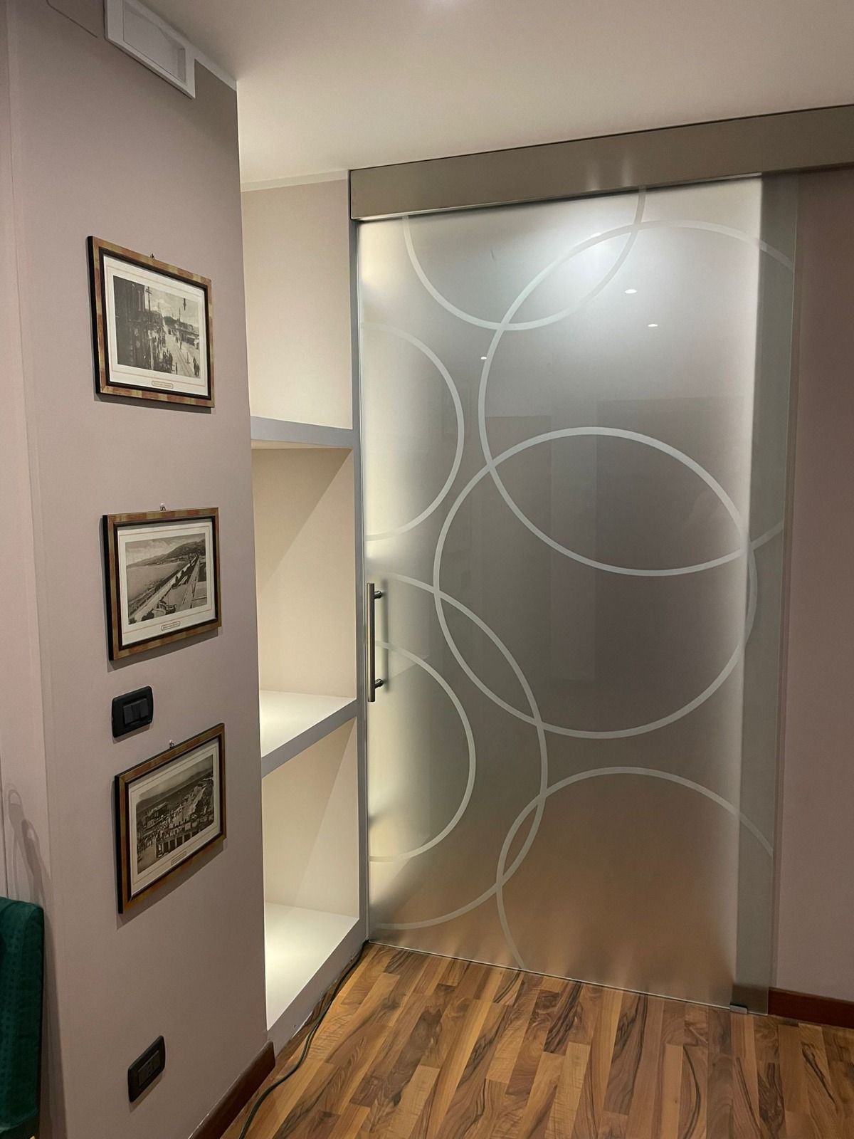 Porta scorrevole in vetro con motivo a cerchi bianchi, accanto a mensole integrate e foto incorniciate su una parete viola.
