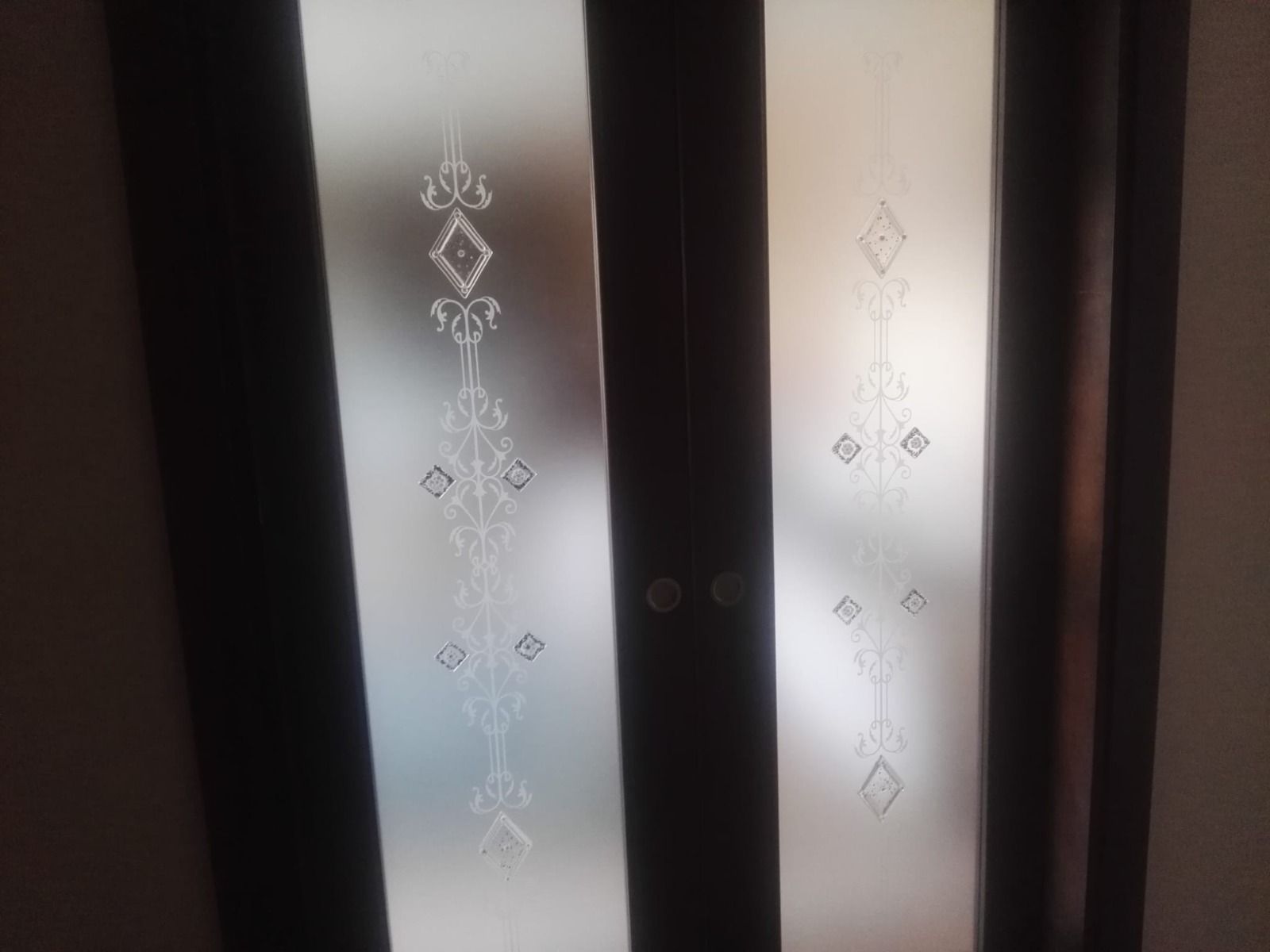 Pannelli delle porte in vetro smerigliato con motivi geometrici incisi in una cornice di legno scuro.