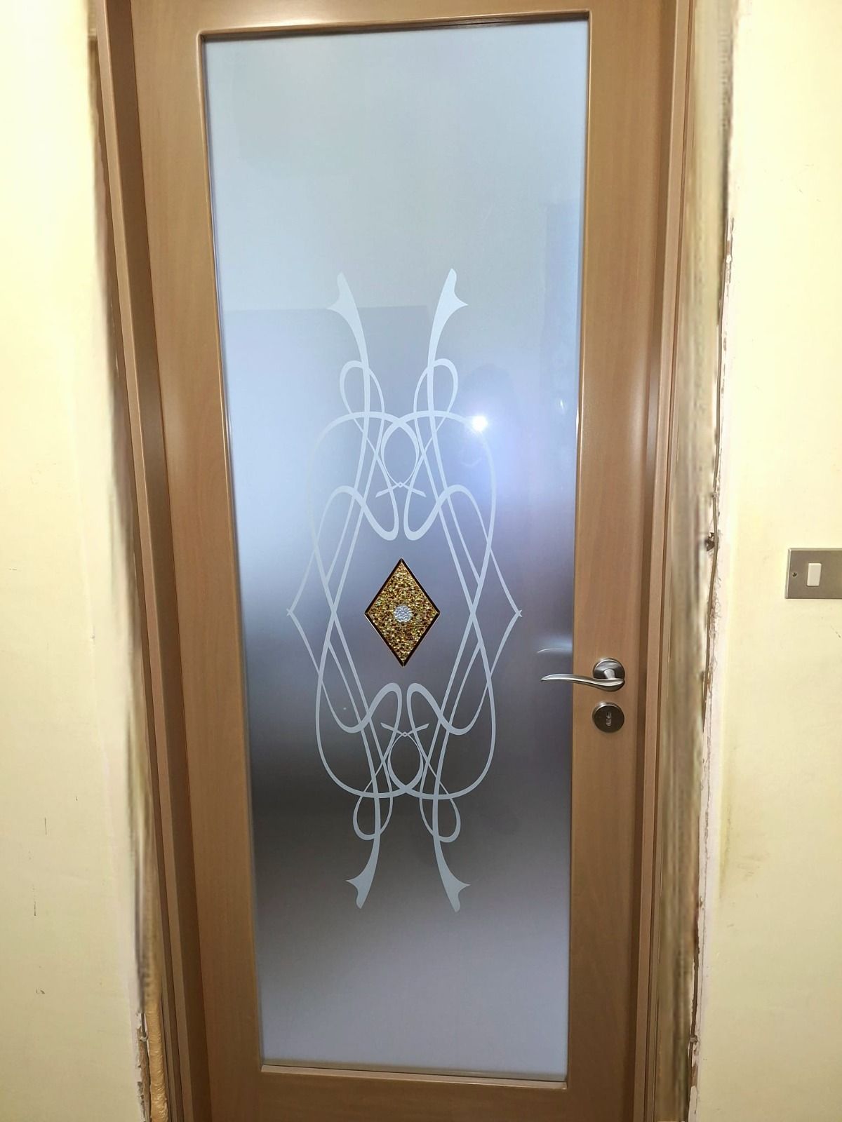Porta marrone con pannello in vetro smerigliato e motivo decorativo bianco e oro.