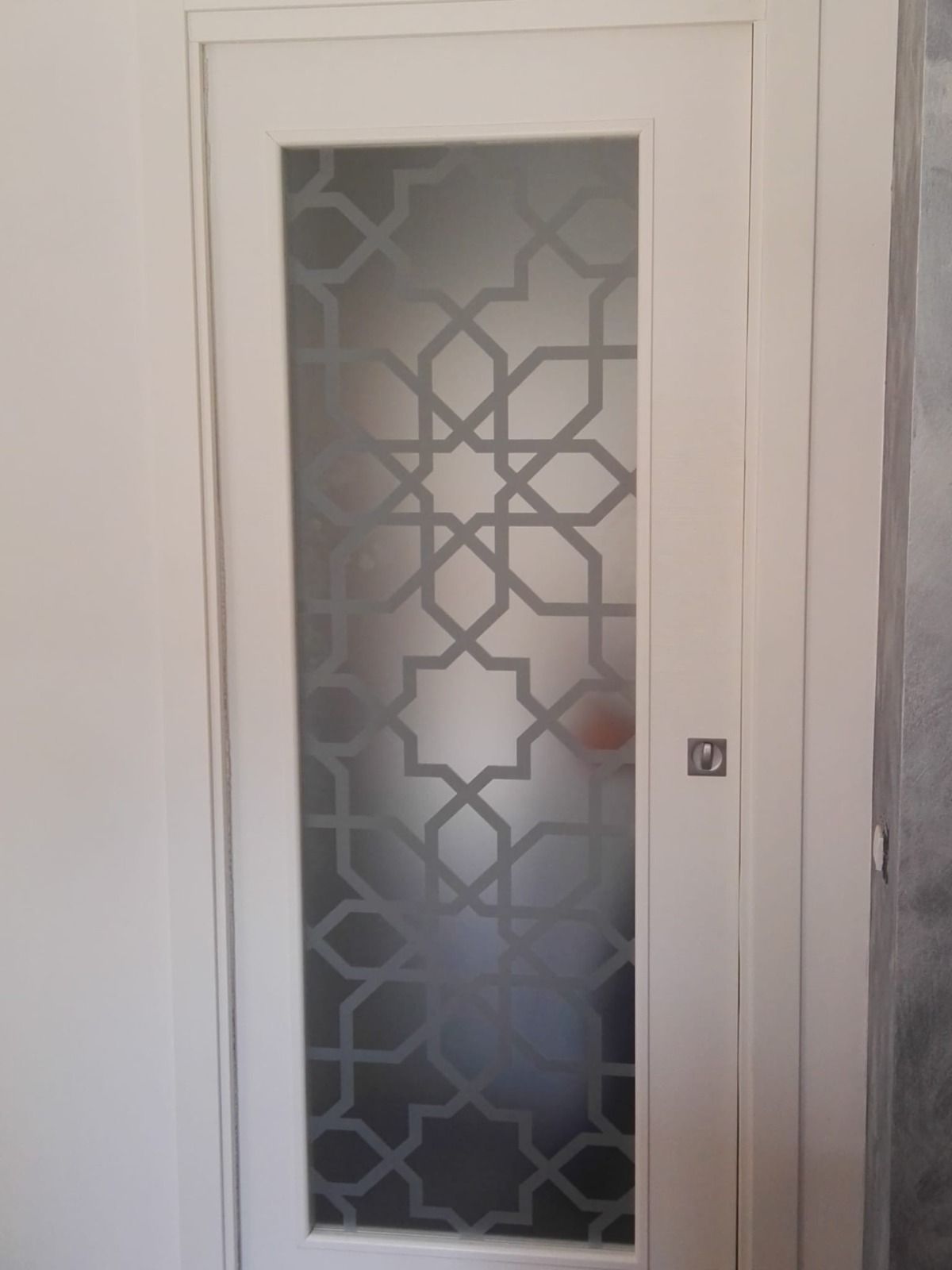 Porta interna bianca con pannello in vetro satinato con motivo geometrico.