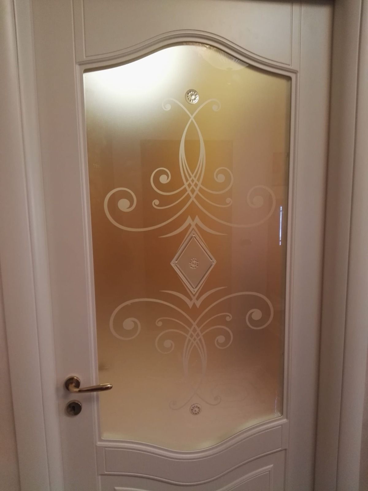 Porta bianca con pannello in vetro smerigliato e motivo decorativo inciso.