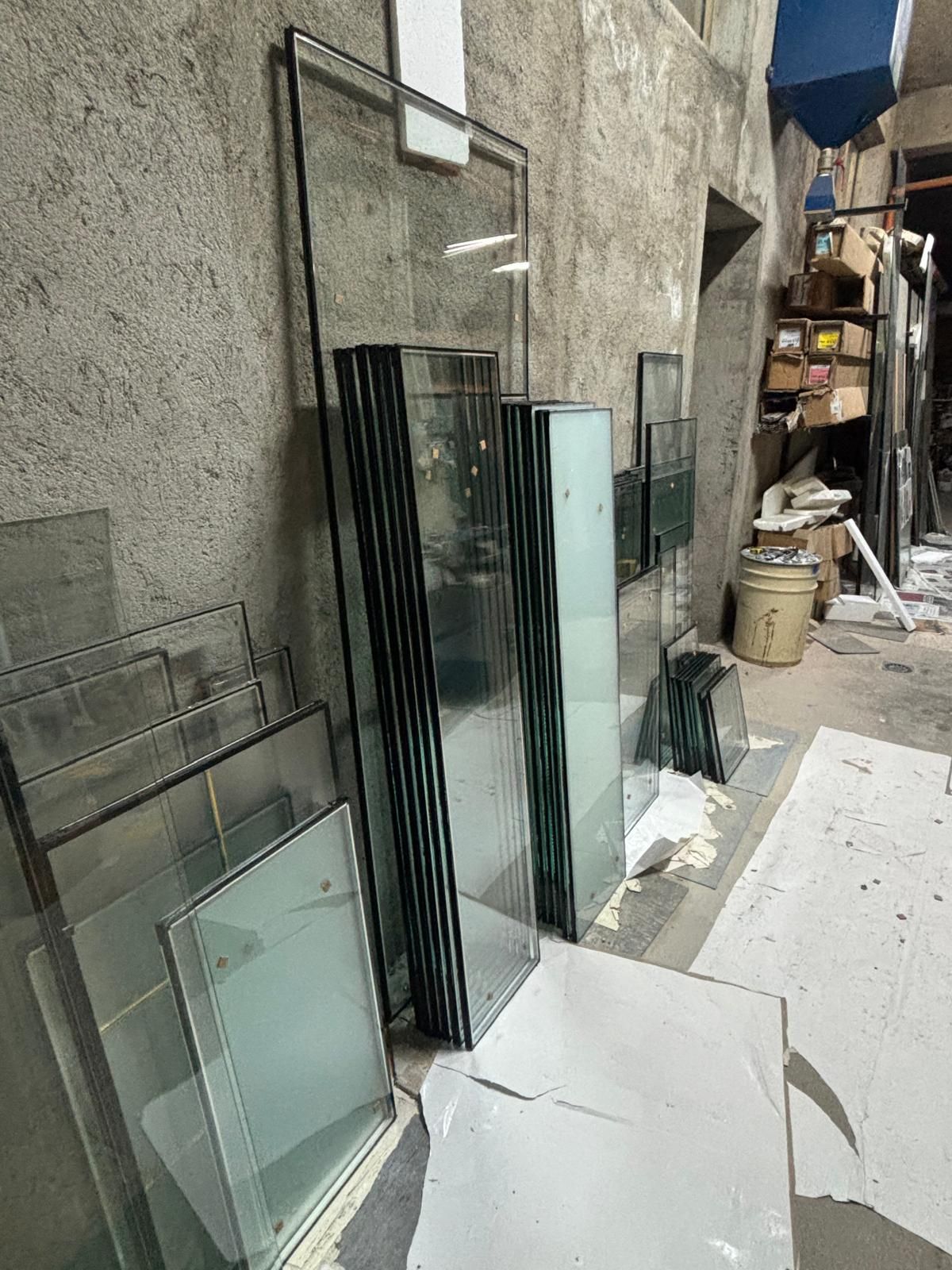 Pile di lastre di vetro rettangolari con cornici nere appoggiate a una parete grigia in un'officina.