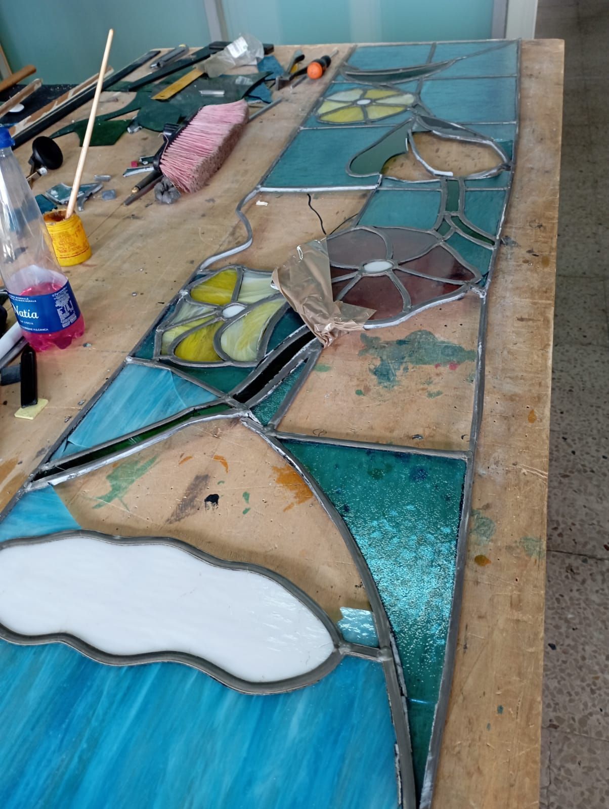 Vetrata con motivi geometrici nei toni del blu, rosso, giallo e verde. La luce filtra attraverso, proiettando ombre colorate.