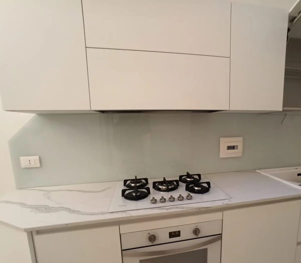 Paraschizzi da cucina in vetro verde acqua con illuminazione da incasso, prese di corrente e piano cottura.