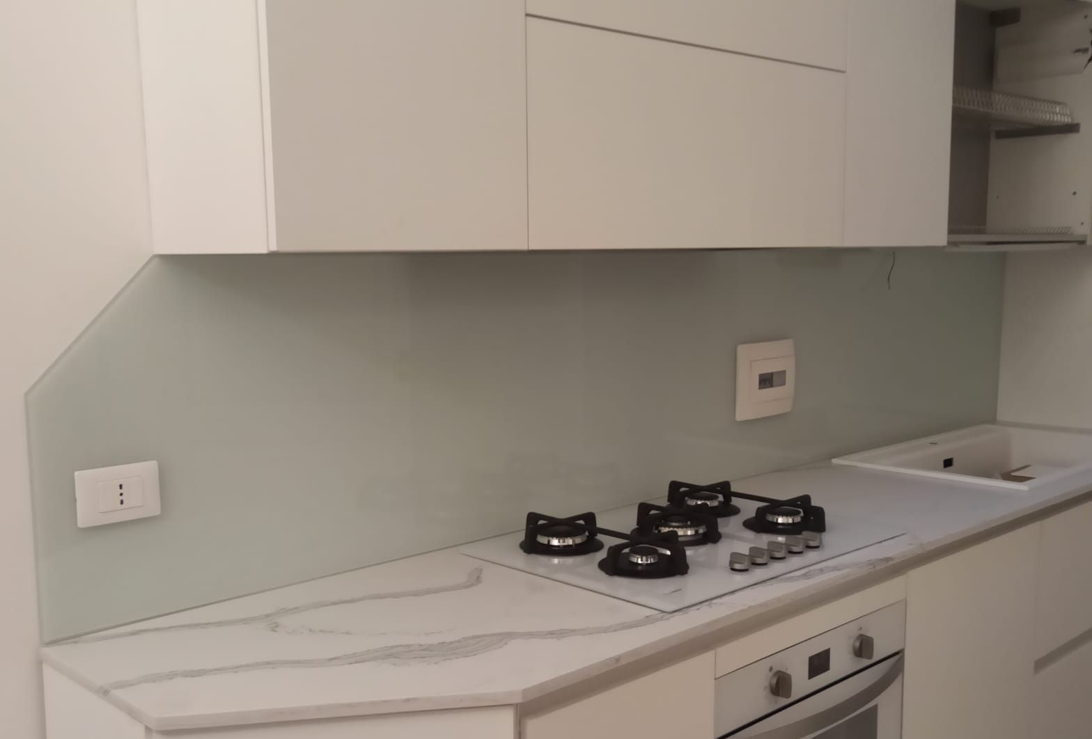 Cucina moderna con mobili verde chiaro, piano di lavoro in legno e rubinetto in acciaio inossidabile.