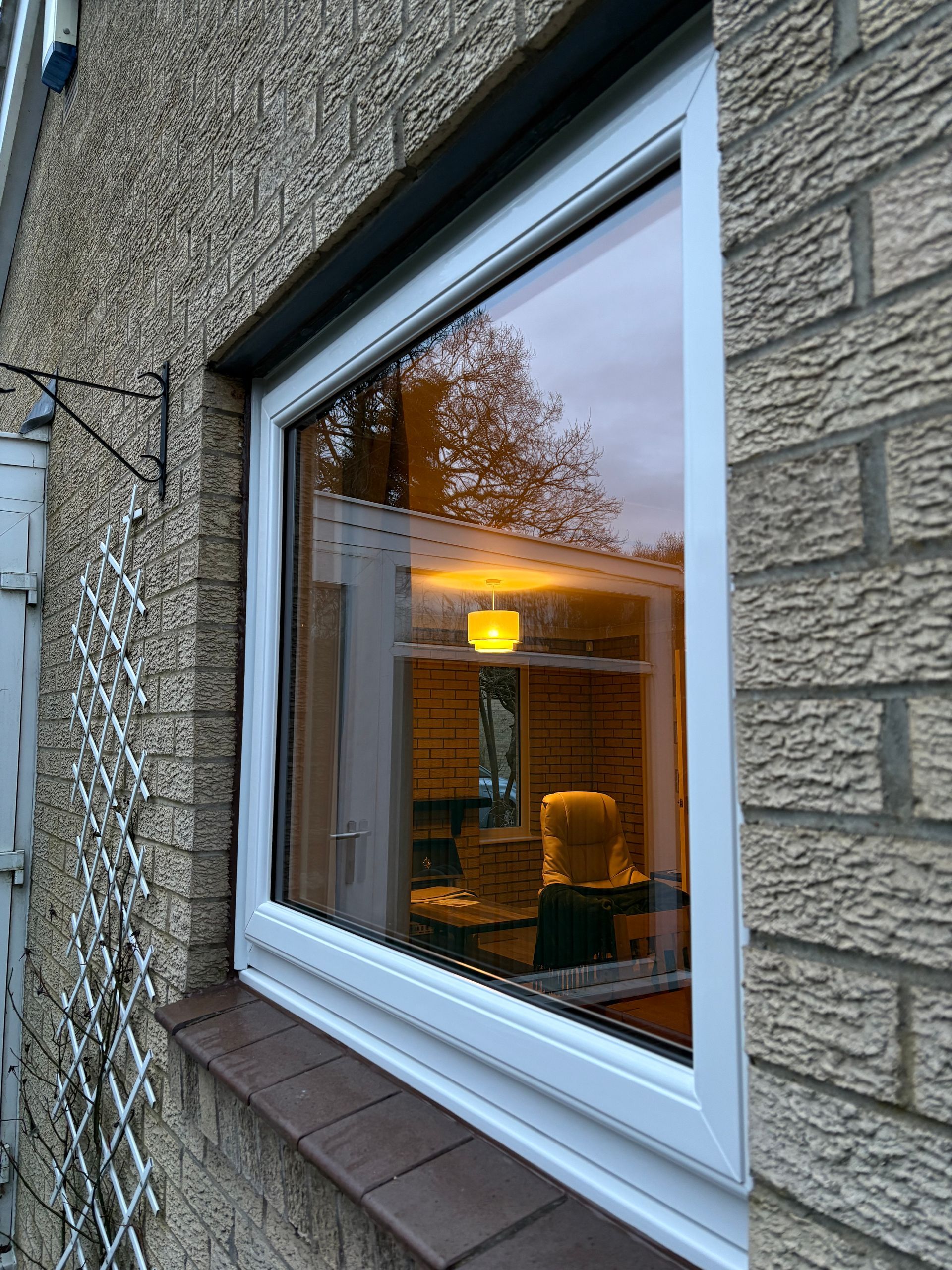 White-framed window reflecting a warm-lit interior, set in a stone brick wall.