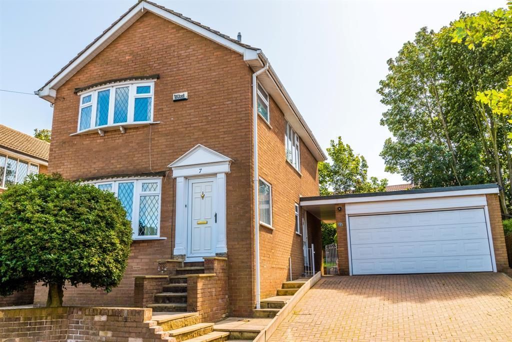 Two-story brick house with a white front door and attached garage. A driveway slopes up to the garage.