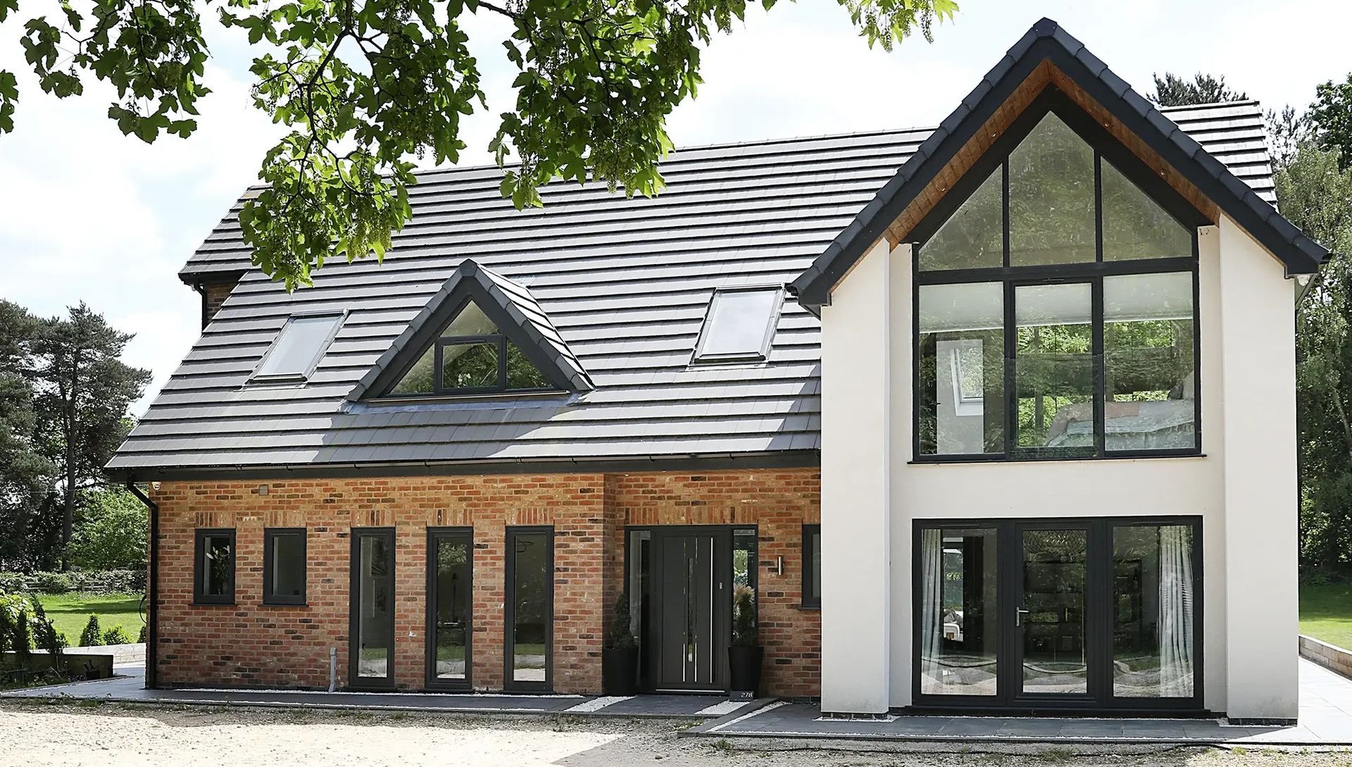 Modern two-story house with brick and white facade. Features large windows, a grey tiled roof