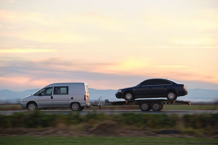 a white van towing a black car on a trailer