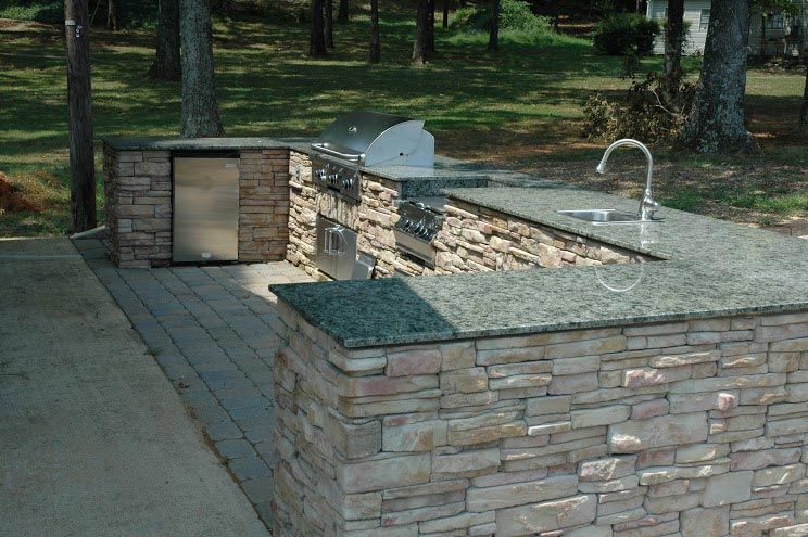 An outdoor kitchen with granite counter tops and a stainless steel grill
