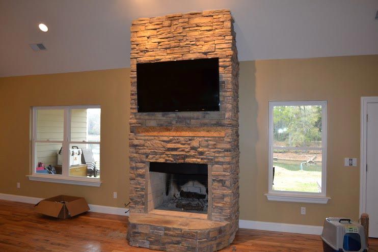 A living room with a stone fireplace and a flat screen tv.