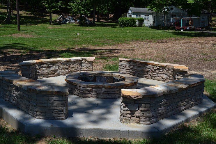 A stone fire pit in a park with a house in the background.