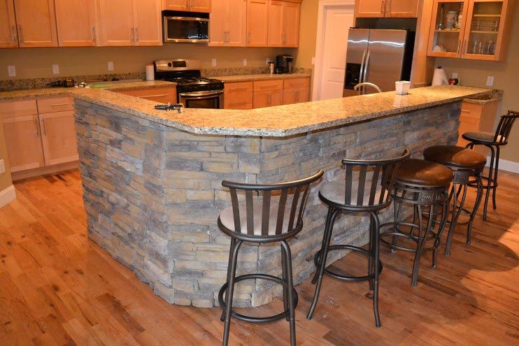 A kitchen with a large stone bar and stools.