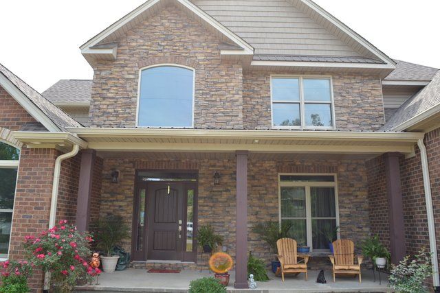A large brick house with a porch and chairs in front of it.