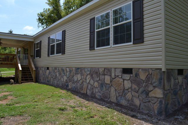 A mobile home with a stone foundation is sitting on top of a lush green field.