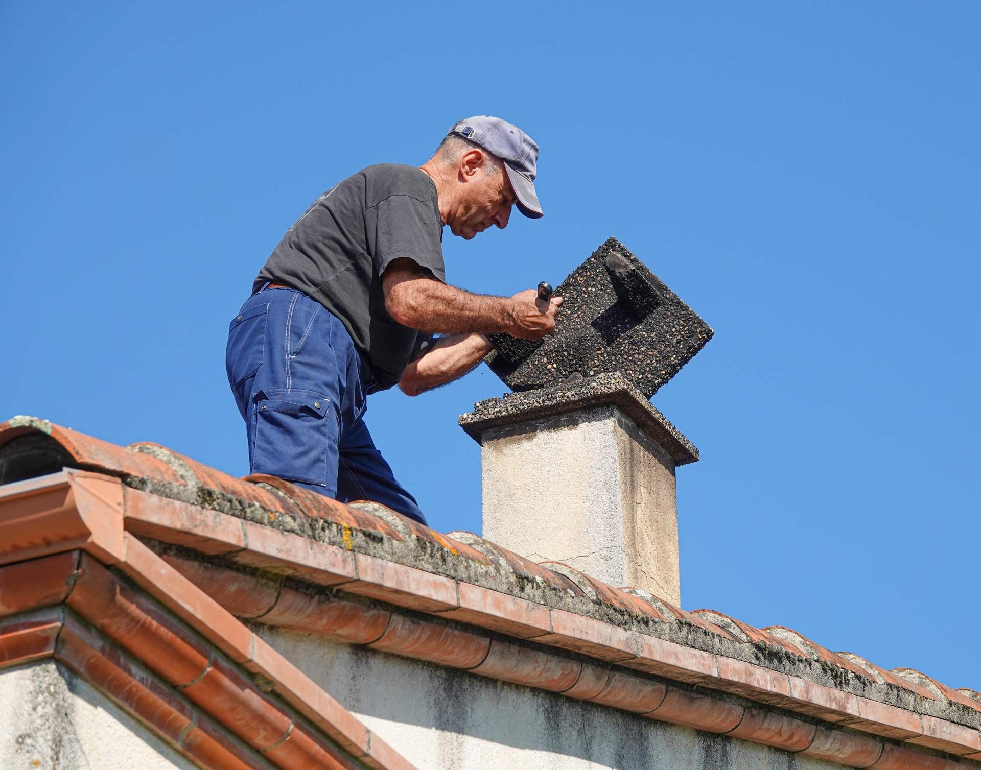 Worker repairing a rooftop chimney against a clear blue sky