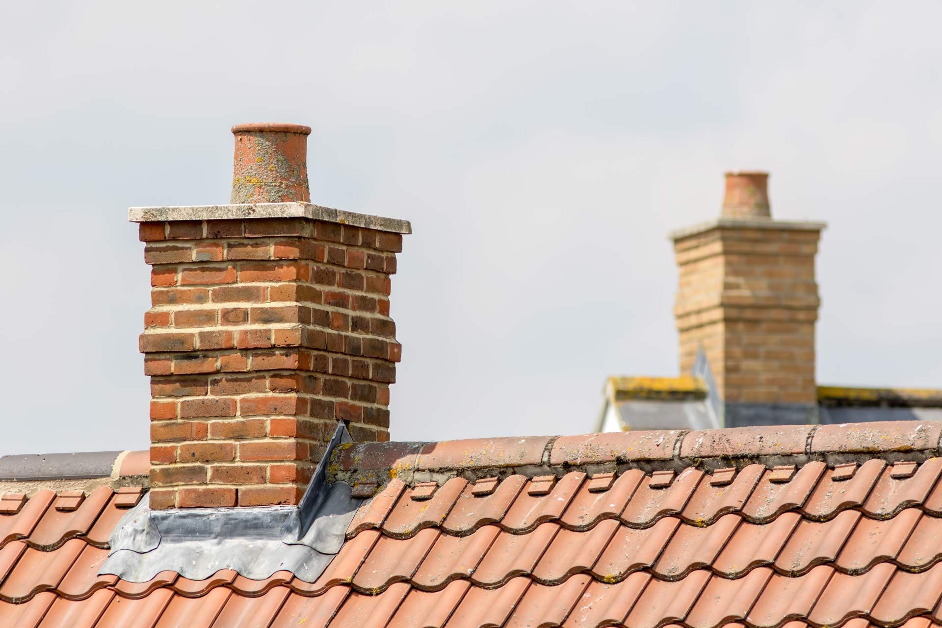 Two brick chimneys rising above a red-tiled roof against a pale sky
