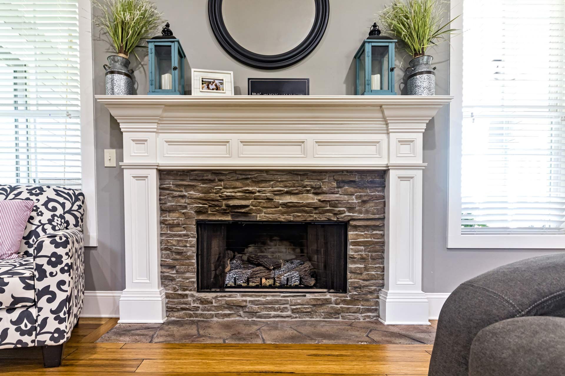 Living room fireplace with white mantel, stone surround, decor, and hardwood floor