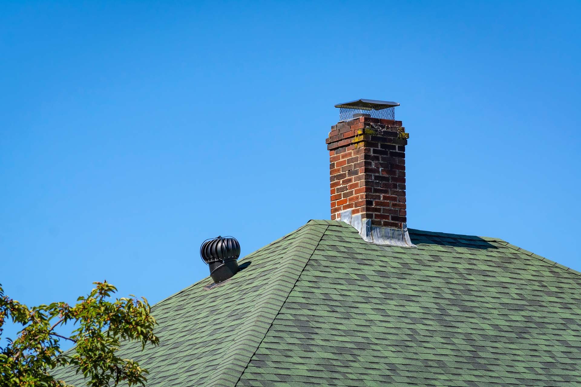Green shingled roof with a brick chimney against a clear blue sky