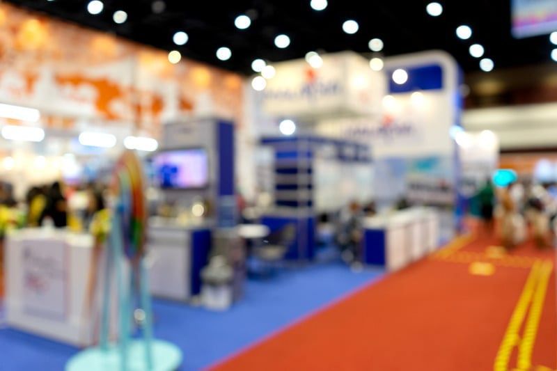 Blurred view of a trade show with booths, red carpet, and blue and white displays.