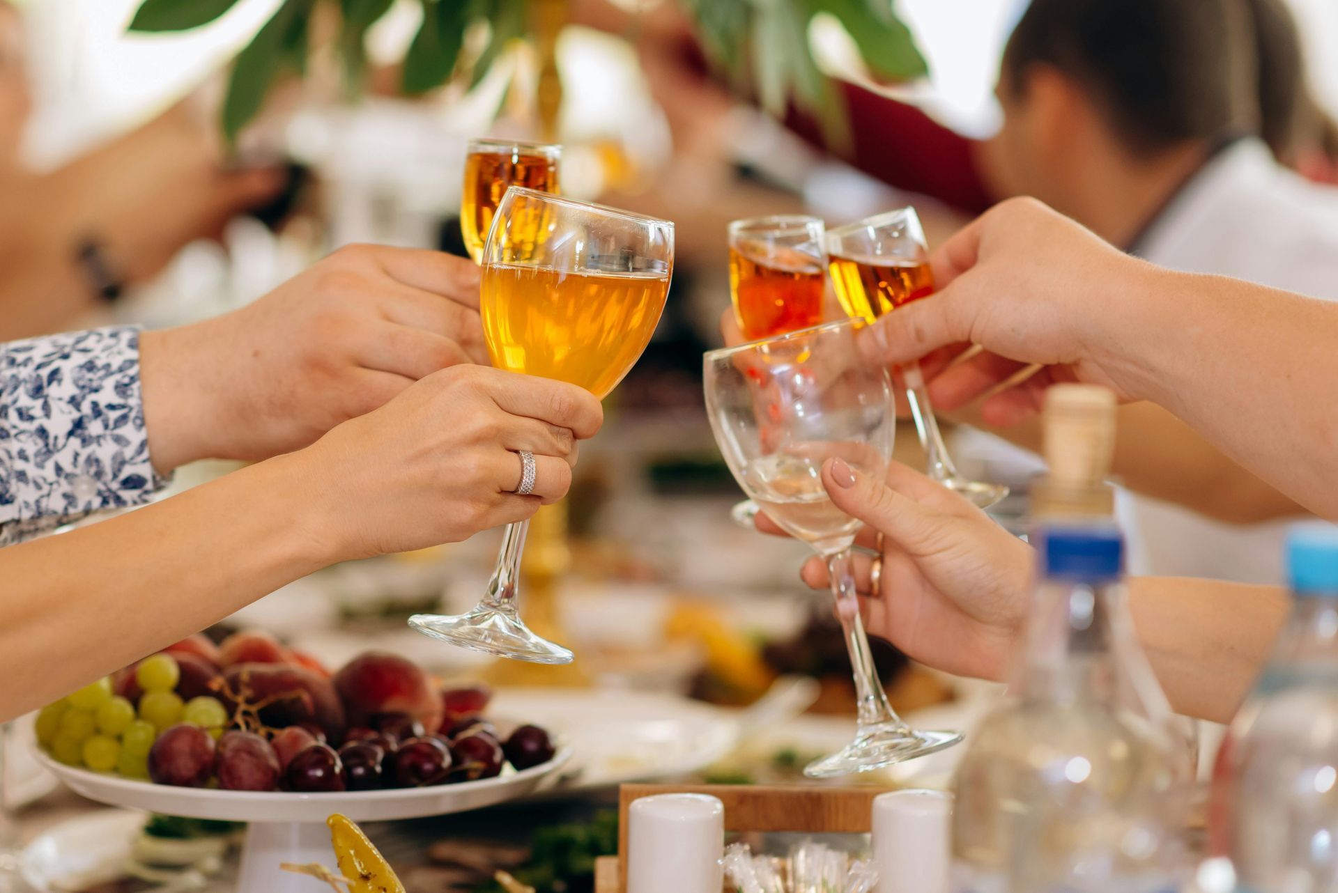 People toasting with glasses of amber-colored drinks at a celebration. A table of food is in the foreground.