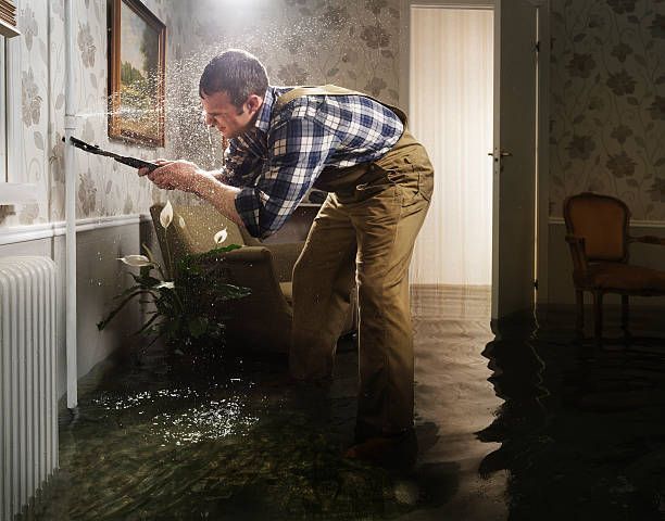 An emergency residential plumber is fixing a pipe in a flooded room.