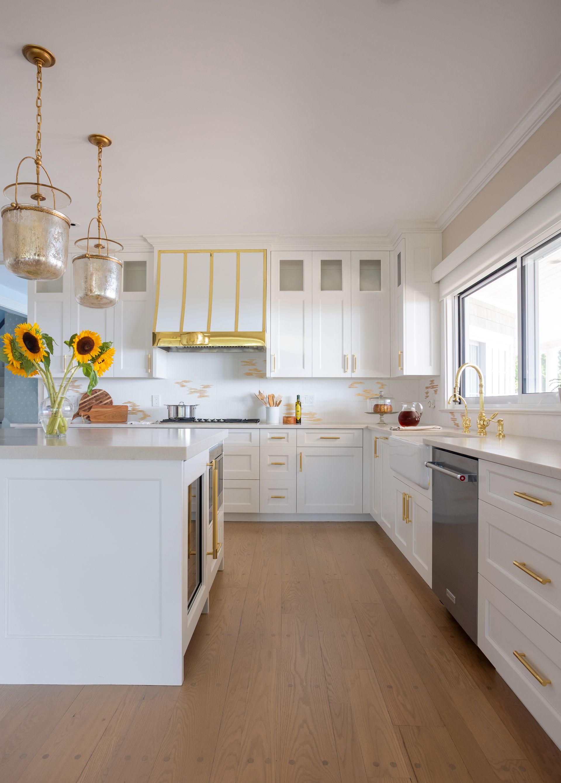 A kitchen with white cabinets and wooden floors and sunflowers on the counter.