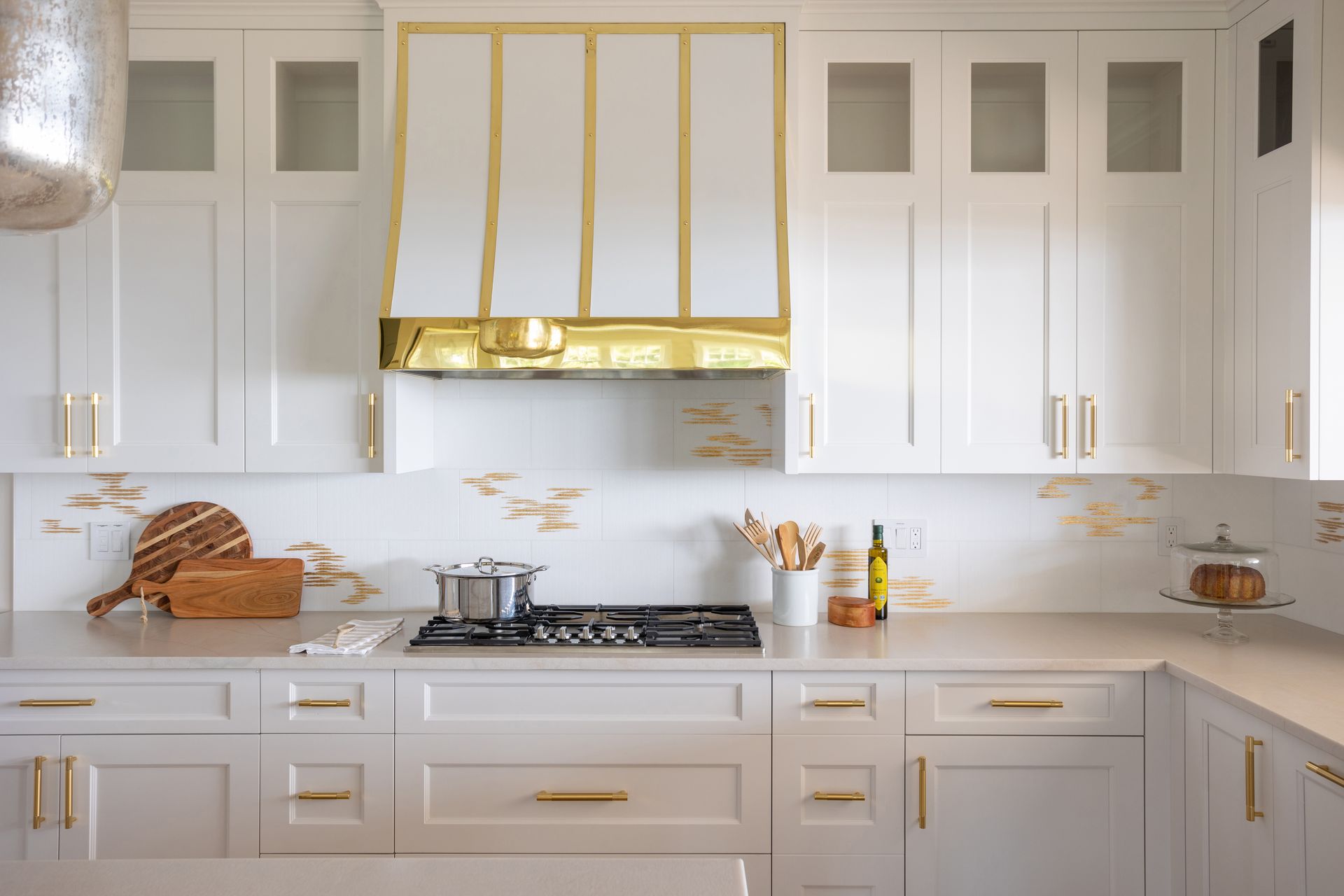 A kitchen with white cabinets and gold trim and a stove top oven.