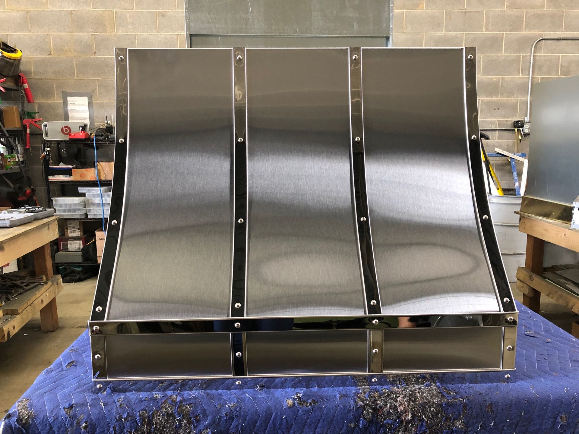 A stainless steel hood is sitting on a blue table.