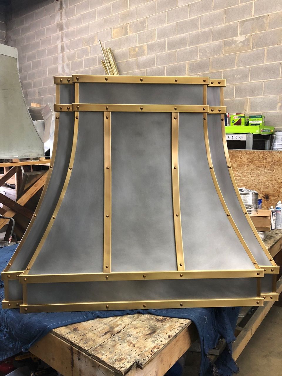 A metal hood with brass trim is sitting on a wooden table.
