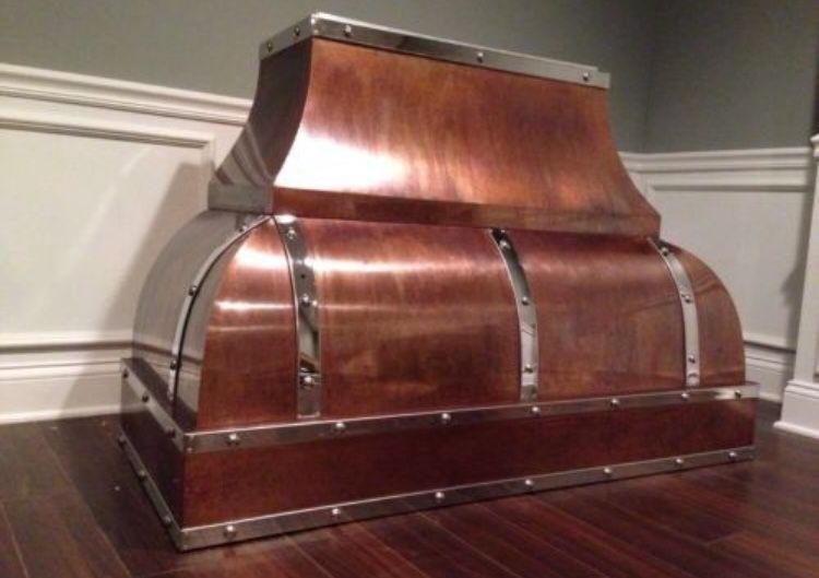 A copper hood is sitting on a wooden floor in a room.