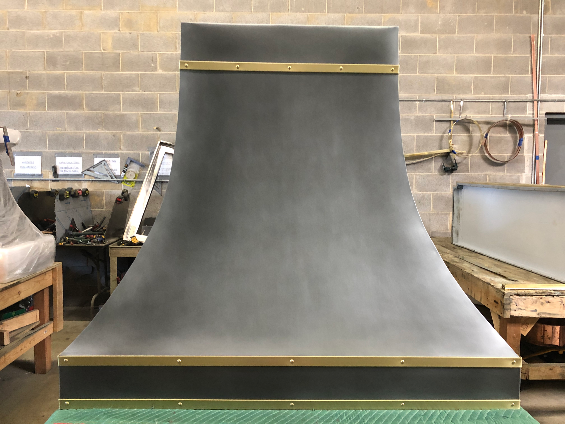 A gray hood with brass trim is sitting on a green table in a room.