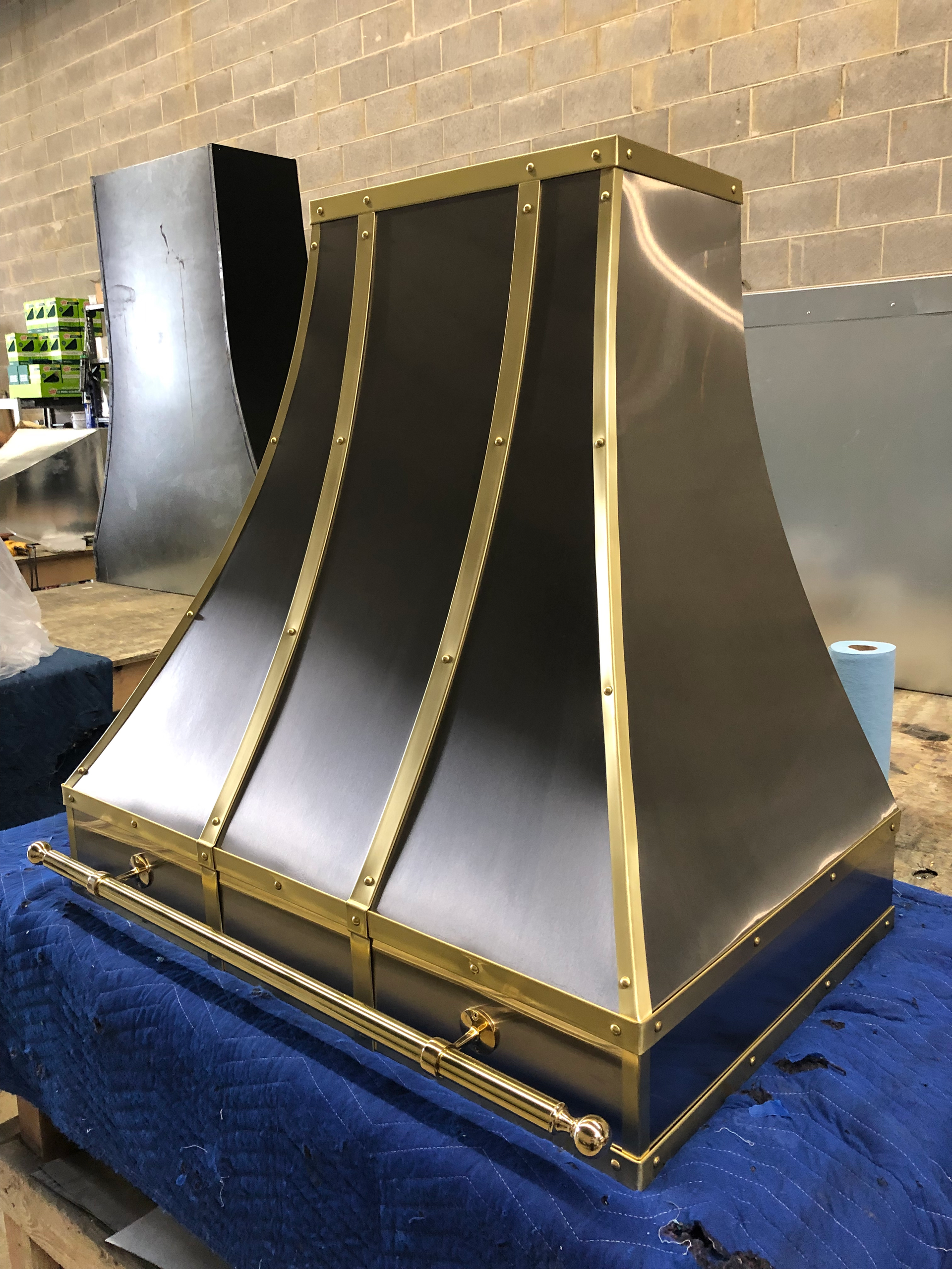 A stainless steel hood with gold trim is sitting on a blue table.