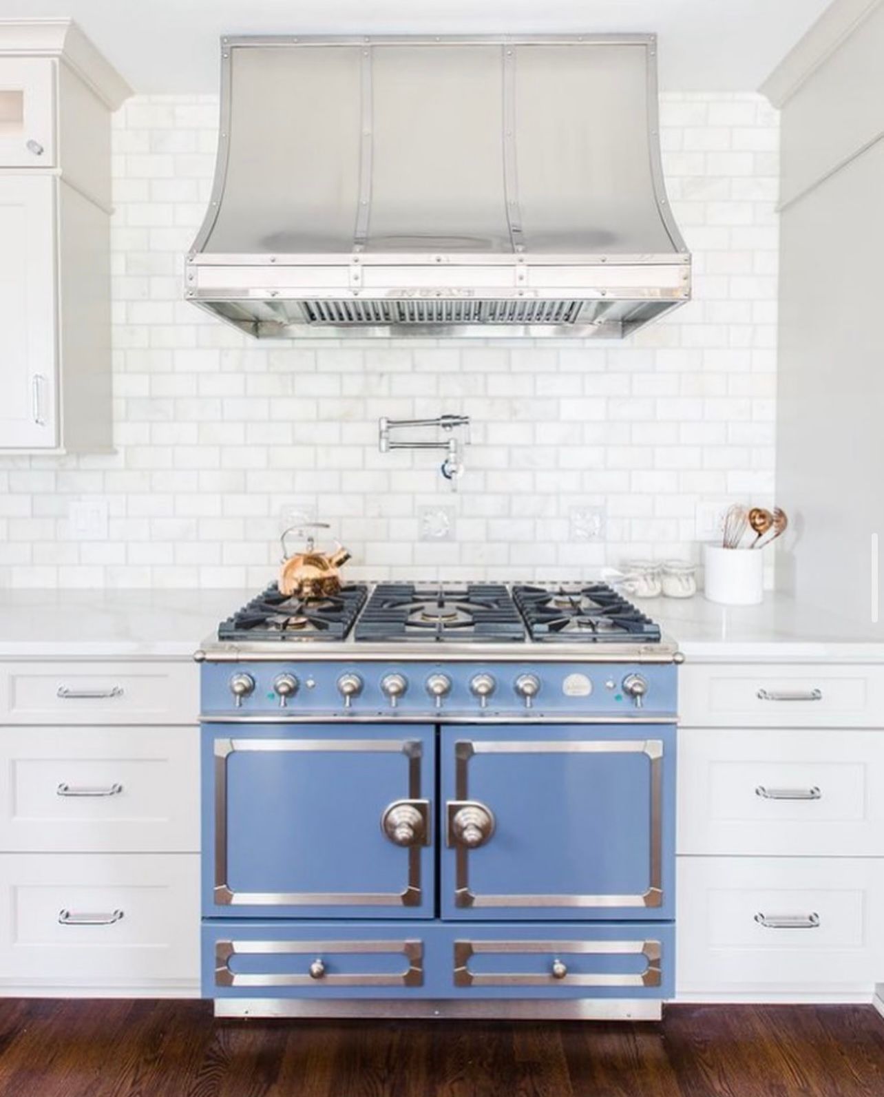A blue stove in a kitchen with white cabinets and a stainless steel hood.