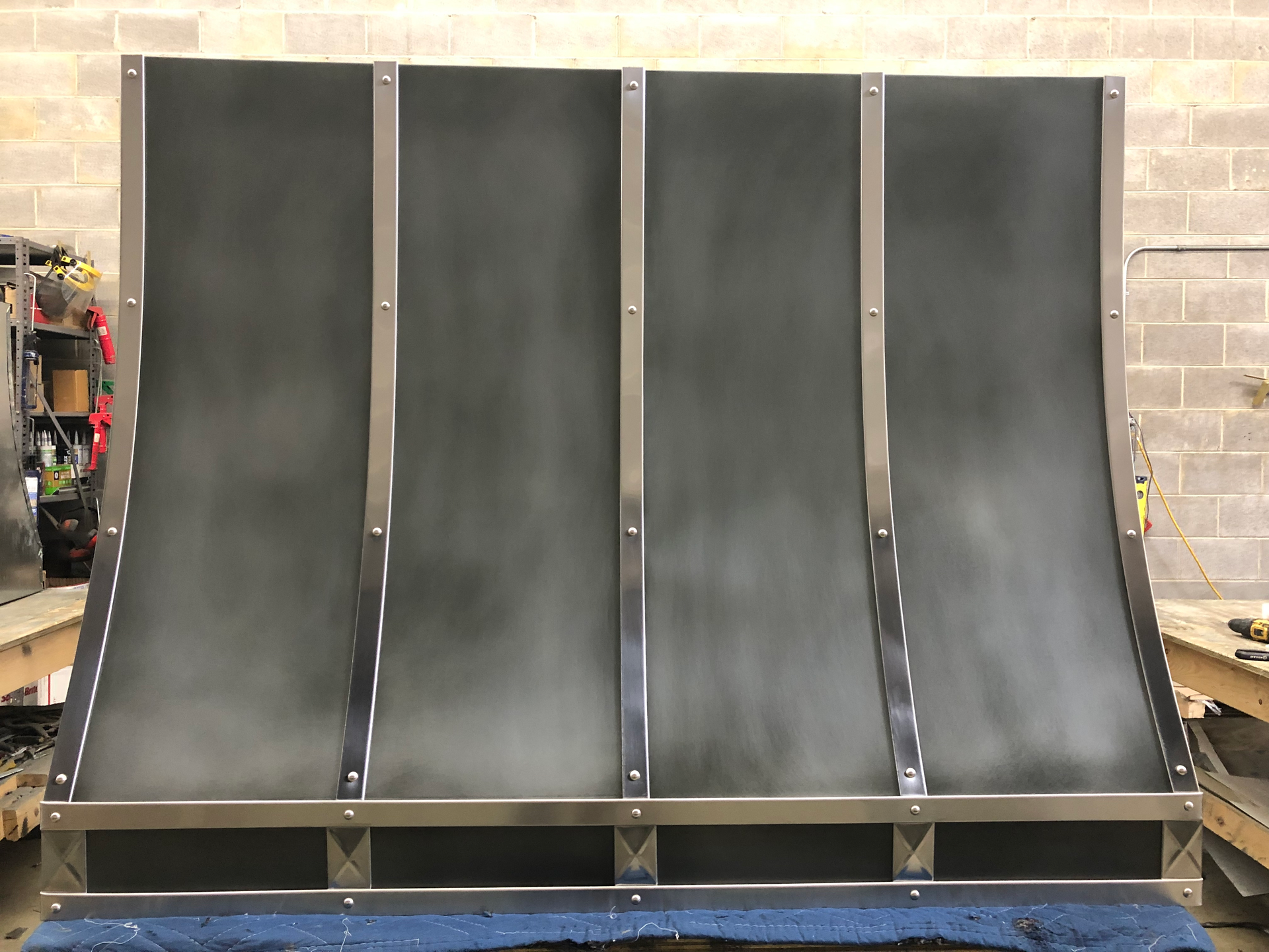 A stainless steel hood is sitting on a blue cloth in front of a brick wall.