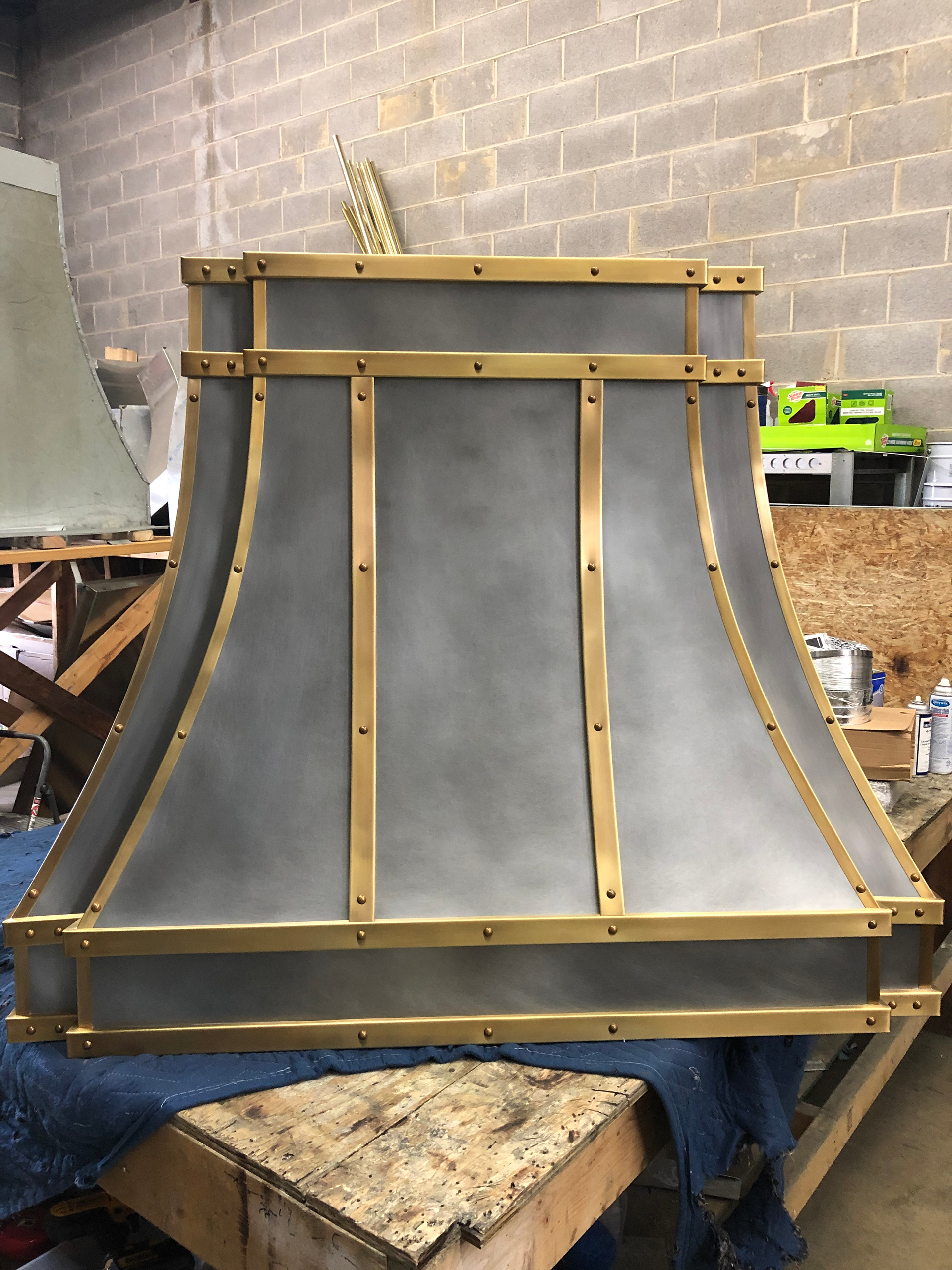 A metal hood with brass trim is sitting on a wooden table.