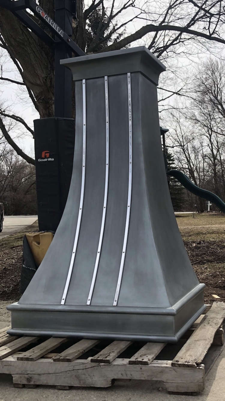 A large metal chimney is sitting on top of a wooden pallet.